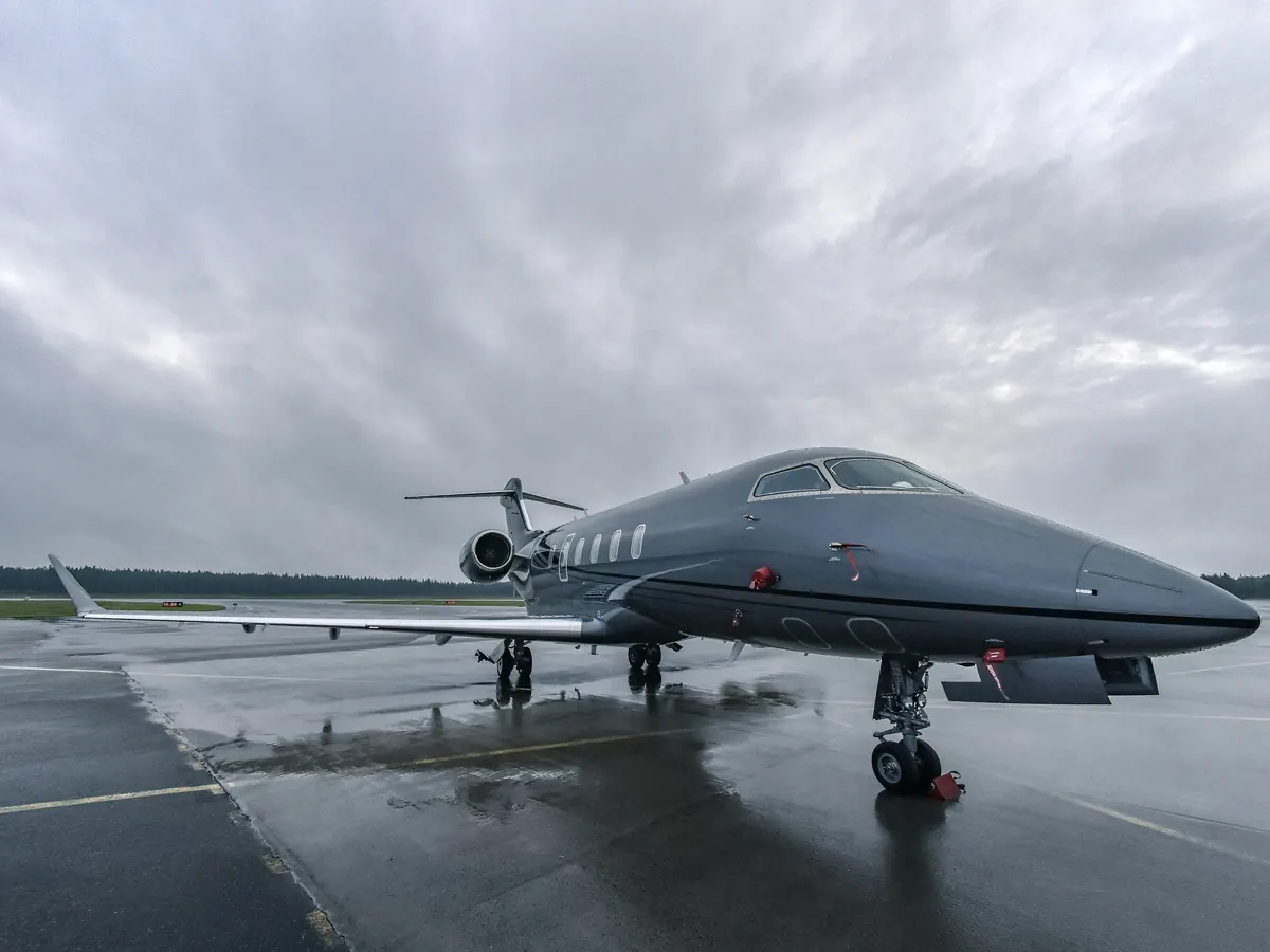 Grey business jet parked on a wet ramp under heavy cloud